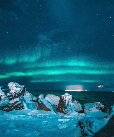 Aurora Borealis seen over the sea in winter from the coast in winter with large rocks piled up in the foreground